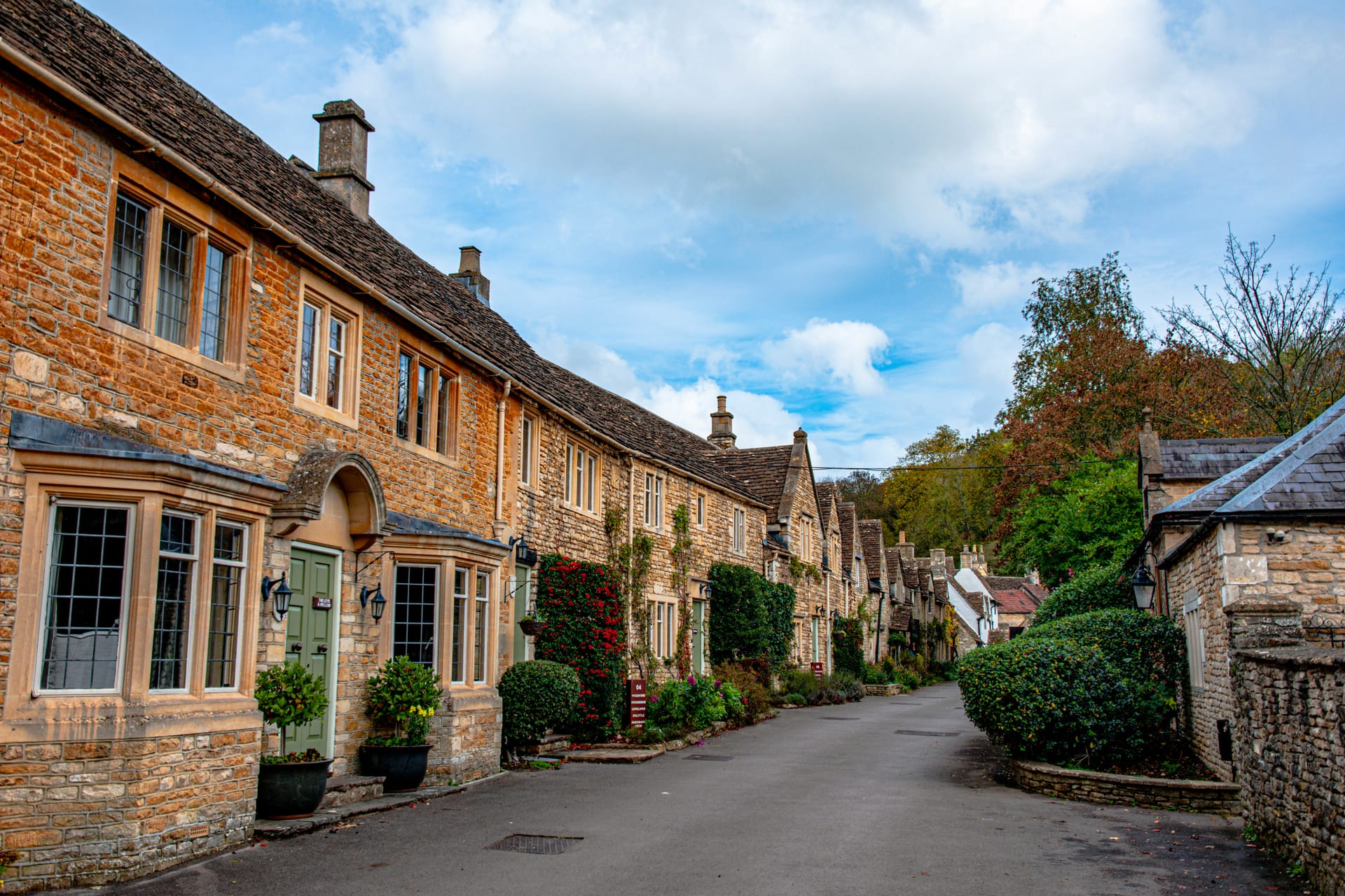 A traditional Cotswolds village with honey-coloured stone cottages, a small stream running through, and a medieval bridge