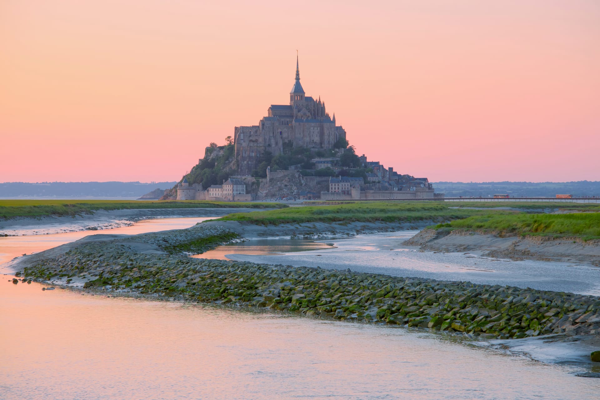 Mont Saint-Michel rising from the tidal bay at sunset, with the abbey silhouetted against an orange sky