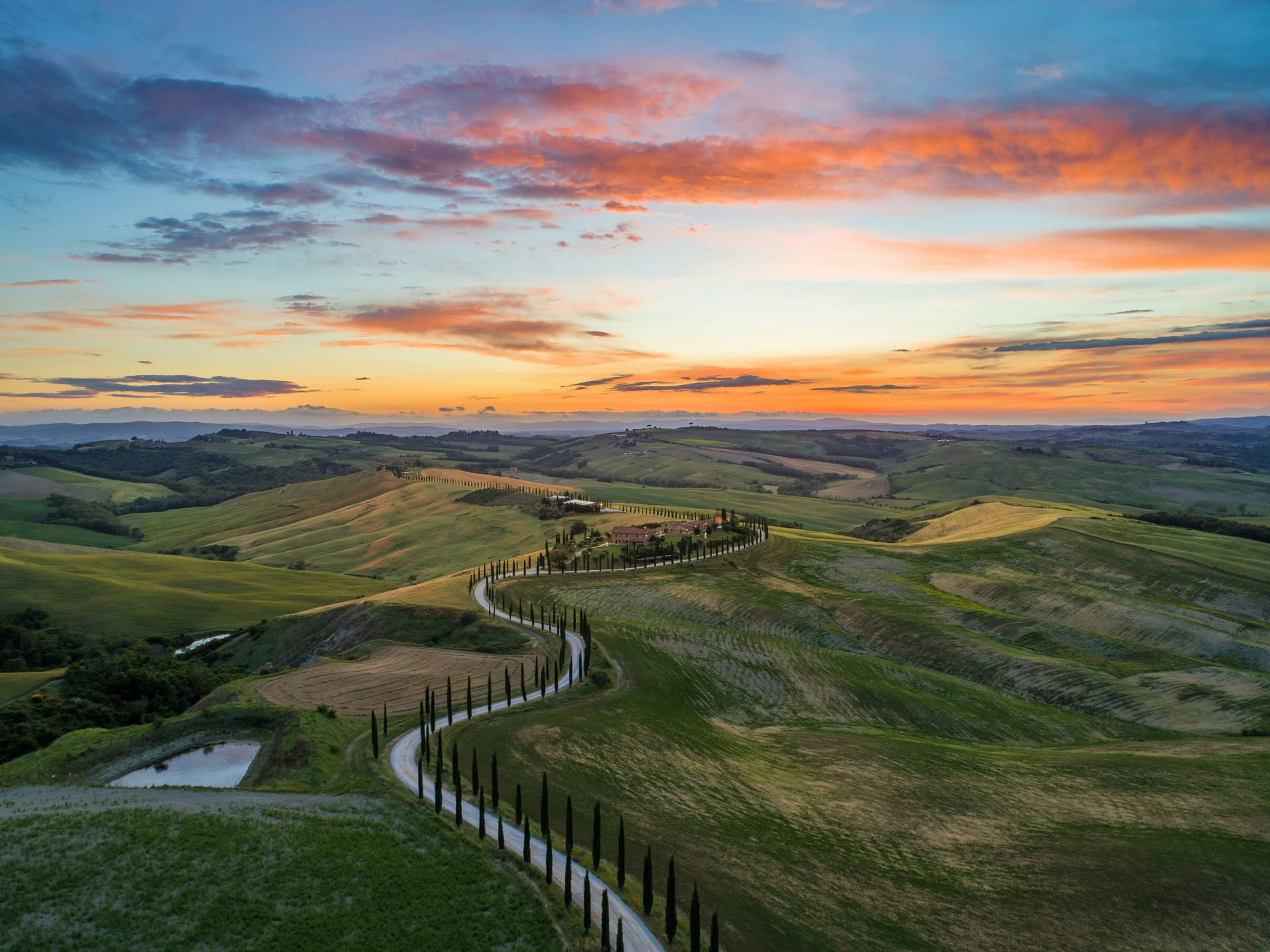 Cypress-lined country road winding through the rolling hills of the Val d'Orcia in Tuscany at sunset